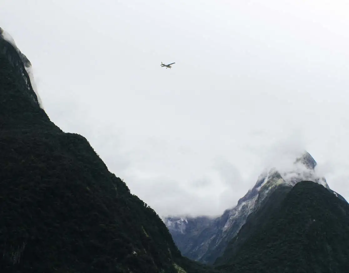Airplane flying between mountains and clouds